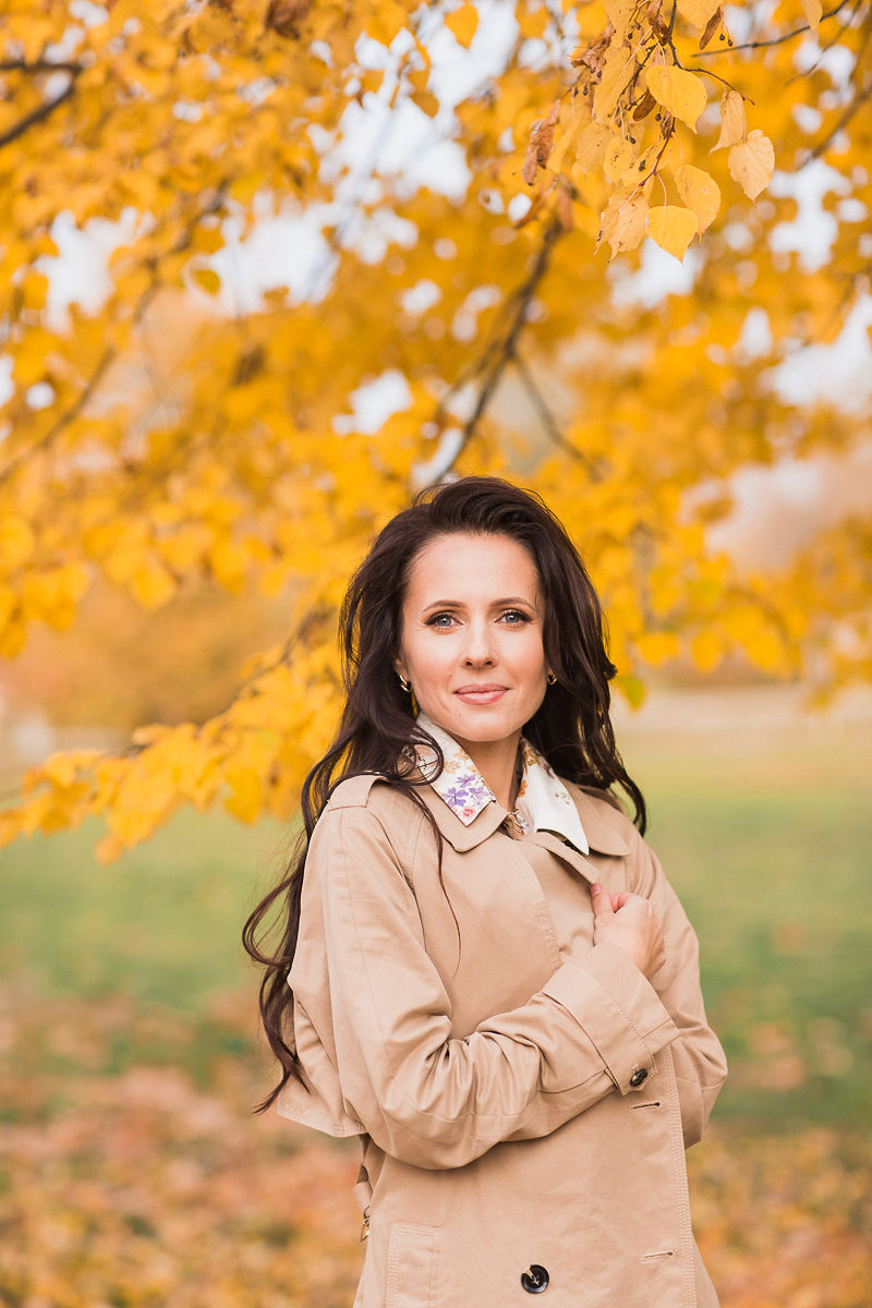 Herbstporträt im beigen Trenchcoat unter goldenen Birkenblättern, sanftes Glam-Make-up von Elena Potapenko