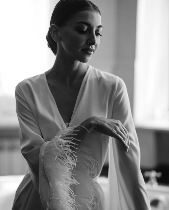 Portrait en noir et blanc d’une mariée en peignoir à manchettes de plumes