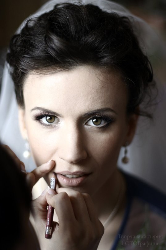 Mariée au maquillage des yeux intense pendant la pose du crayon à lèvres