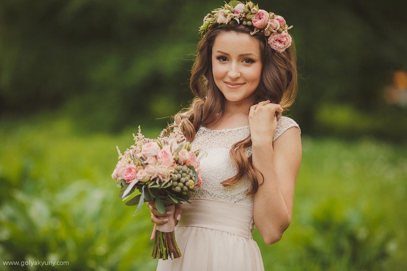 Mariée couronnée de fleurs avec un bouquet rose dans une prairie verte