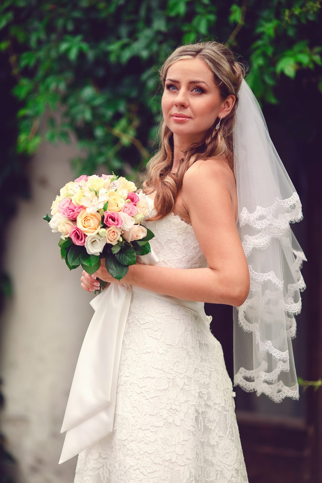 Mariée en robe de dentelle et voile festonné avec un bouquet de roses au jardin