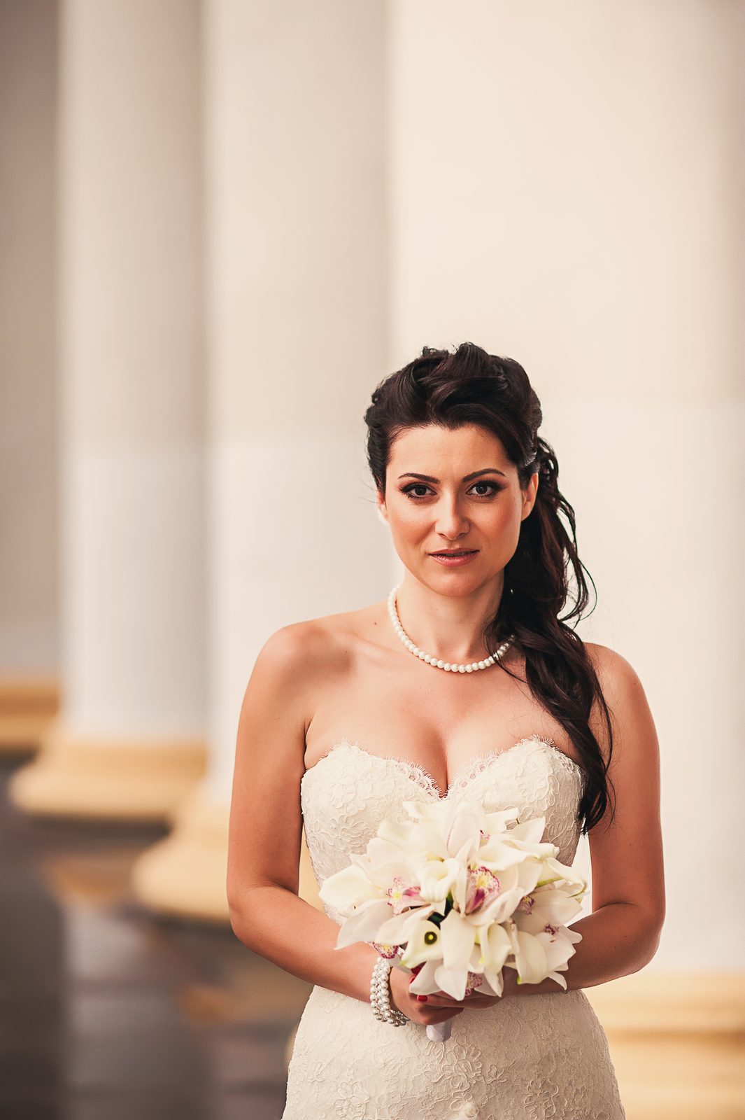 Mariée avec perles et bouquet de lys entre des colonnes blanches