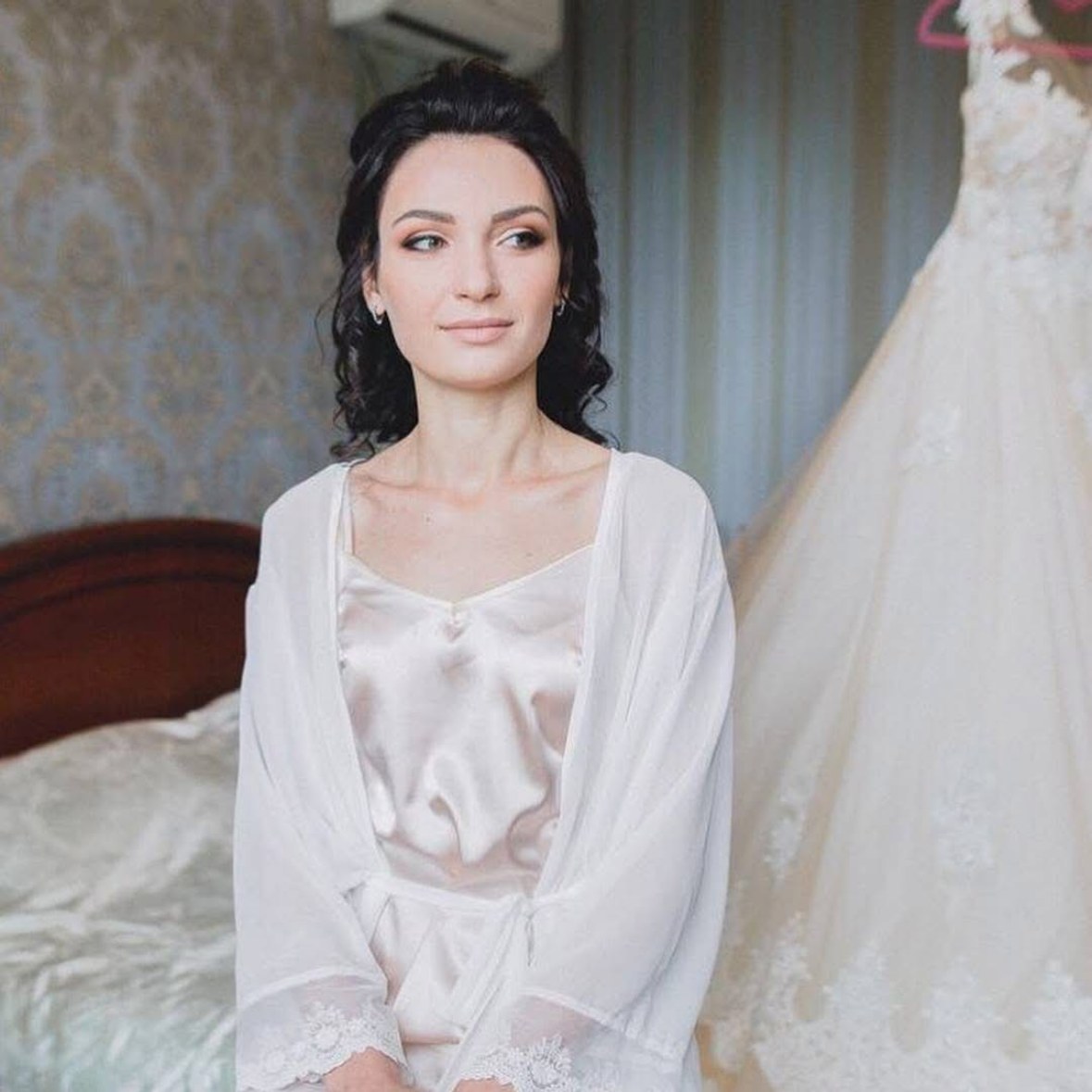 Mariée en peignoir blanc aux ondulations brunes souples, robe de mariée en arrière-plan