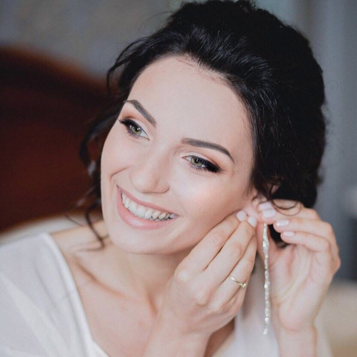 Mariée souriante mettant une boucle d’oreille, chignon de mariée souple