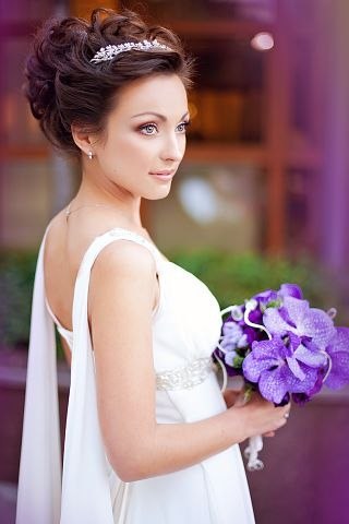 Mariée avec diadème et chignon, bouquet d'orchidées violettes et robe fluide
