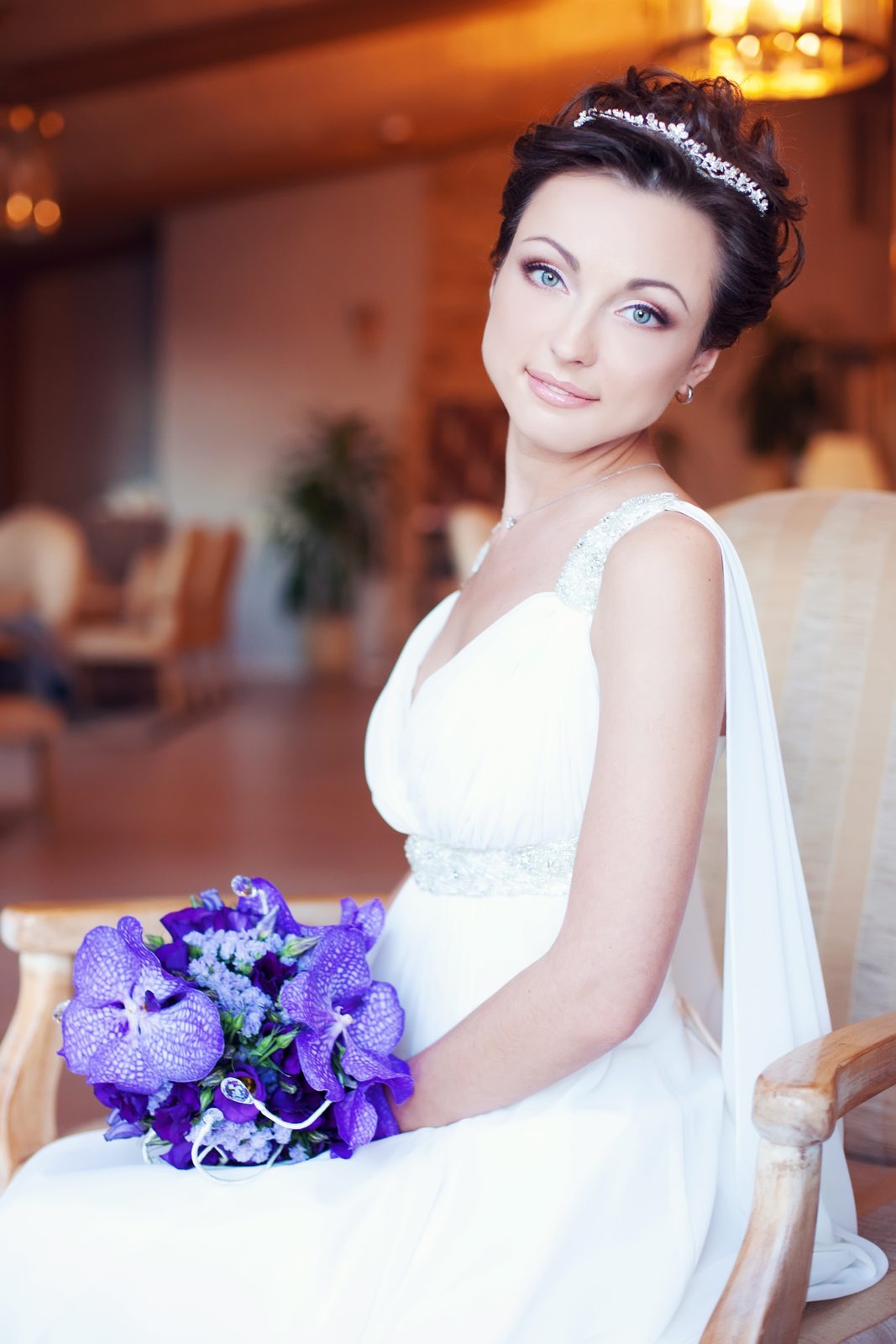 Mariée avec diadème et chignon court, assise avec un bouquet d'orchidées violettes