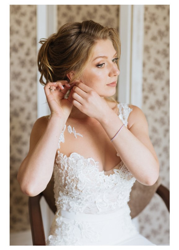 Mariée ajustant une boucle d’oreille, chignon avec robe de mariée en dentelle
